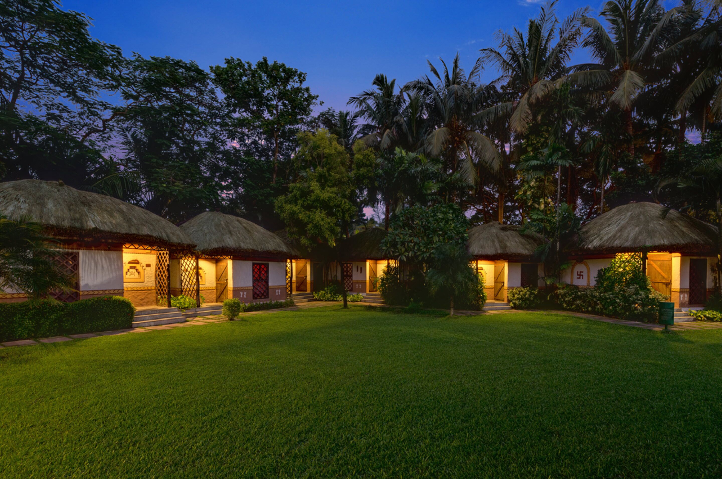 A resort with thatched-roof cottages, a well-maintained lawn, and tropical trees.