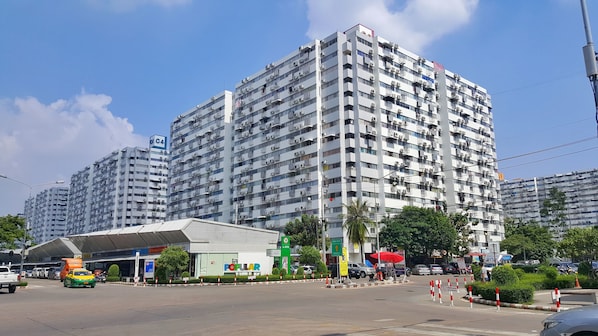 A high-rise residential building with multiple balconies, a covered entrance, and a visible ATM.