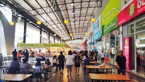A busy indoor market with tables and chairs, people walking, and various shops. - Popular Condo Muangthong Thani (Pak Kret)