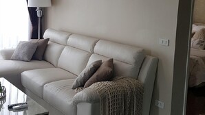 A modern living room with a beige sofa, a glass coffee table, and a lamp. - Popular Condo Muangthong Thani (Pak Kret)