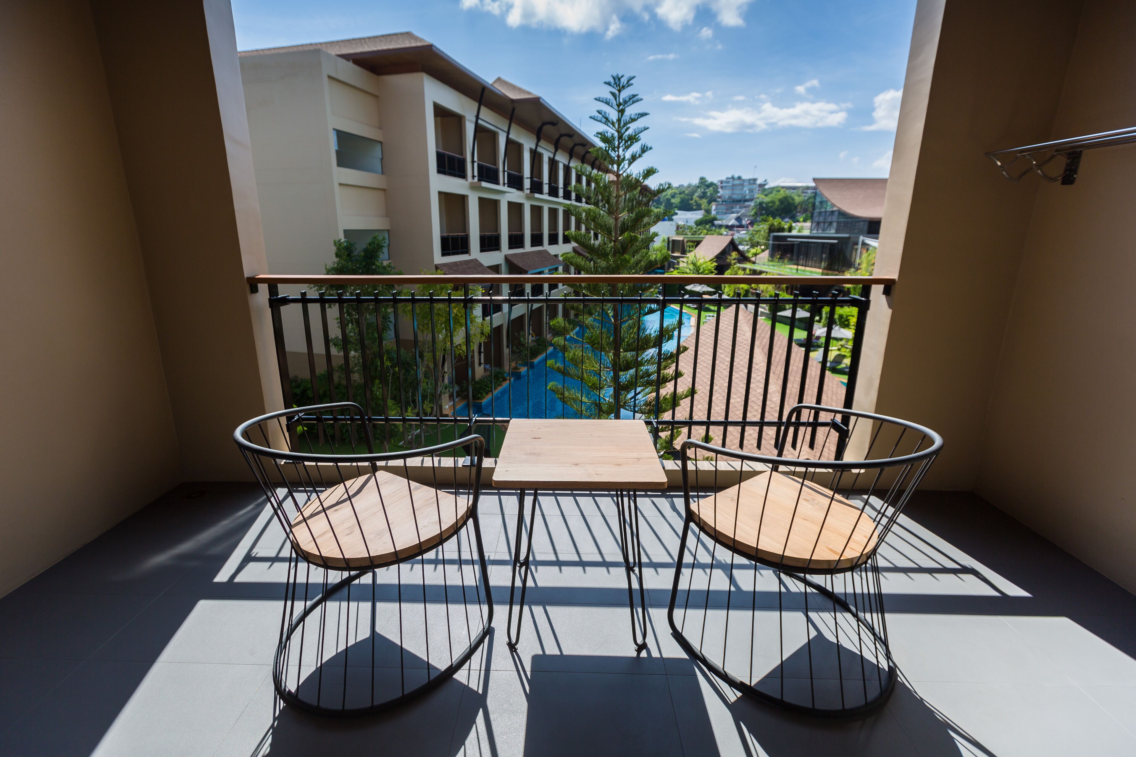 Ein Balkon mit zwei Stühlen und einem Tisch, mit Blick auf einen Pool und Gebäude.
