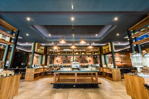 A modern restaurant interior with a central serving table, wooden accents, and hanging pendant lights.