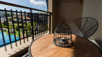 A round wooden table with a metal birdcage on it, a black metal chair, and a view of a swimming pool and greenery through a balcony railing.
