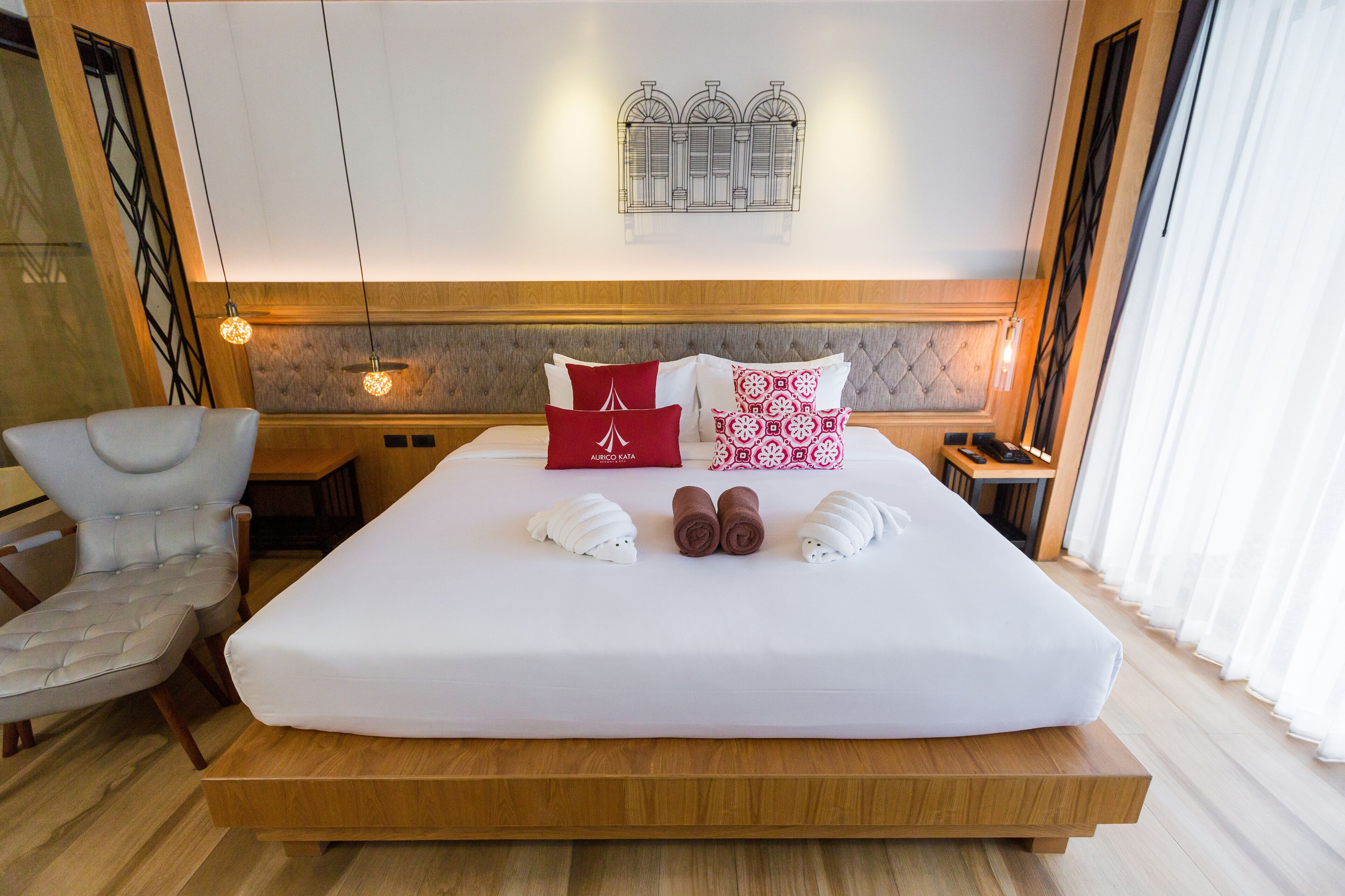 A neatly made bed with white and red pillows, a wooden headboard, and a wall-mounted light fixture.
