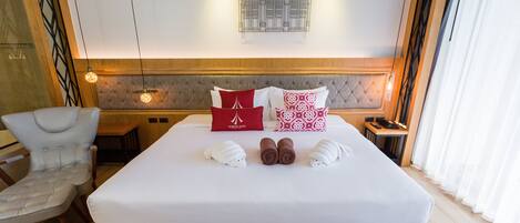 A neatly made bed with white and red pillows, a wooden headboard, and a wall-mounted light fixture.