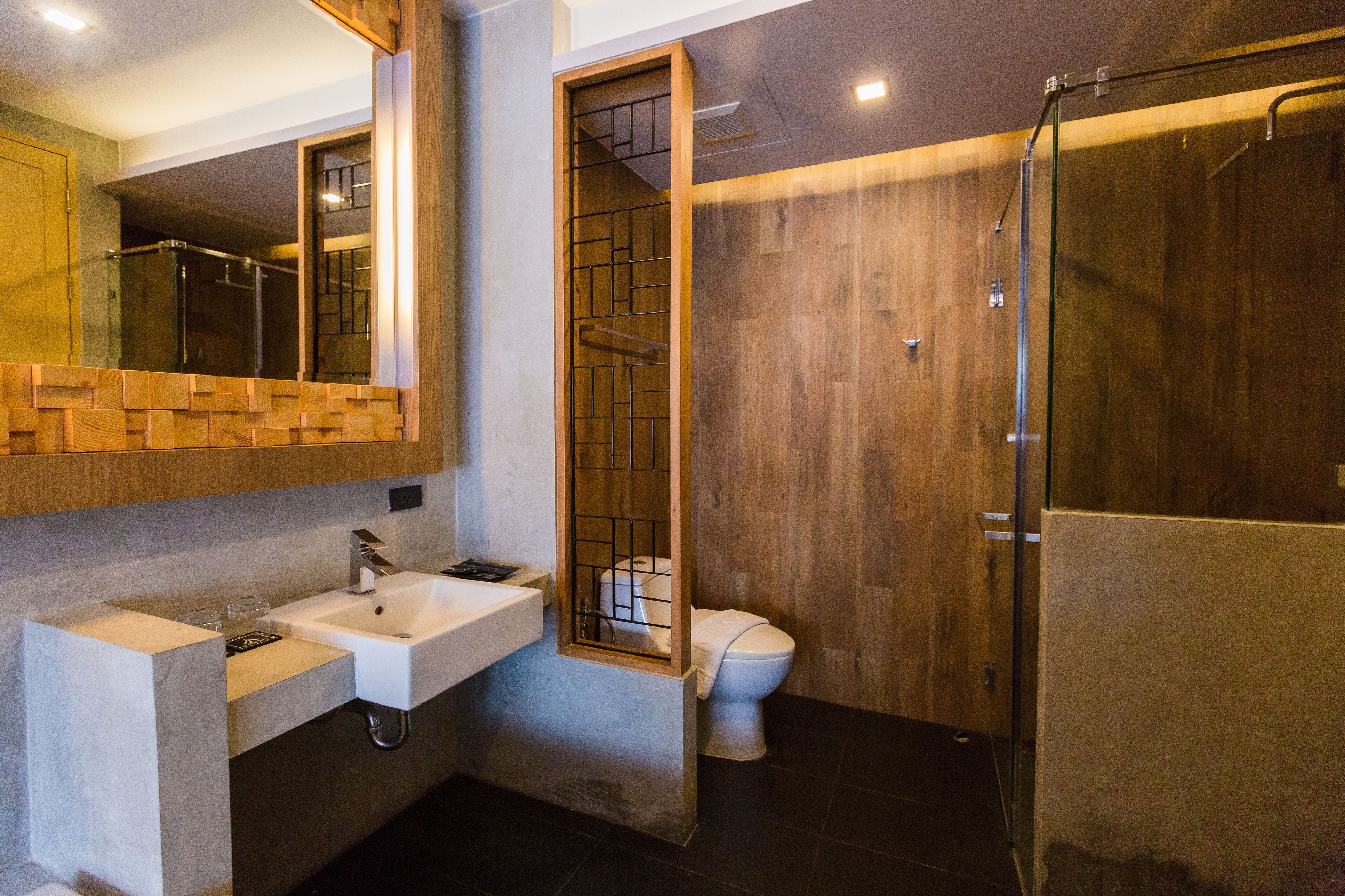 A modern bathroom with a wooden vanity, a toilet, and a glass-enclosed shower.