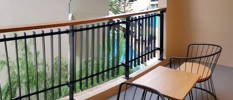 A balcony with a wooden table and two chairs, a metal railing, and a view of a building and greenery.