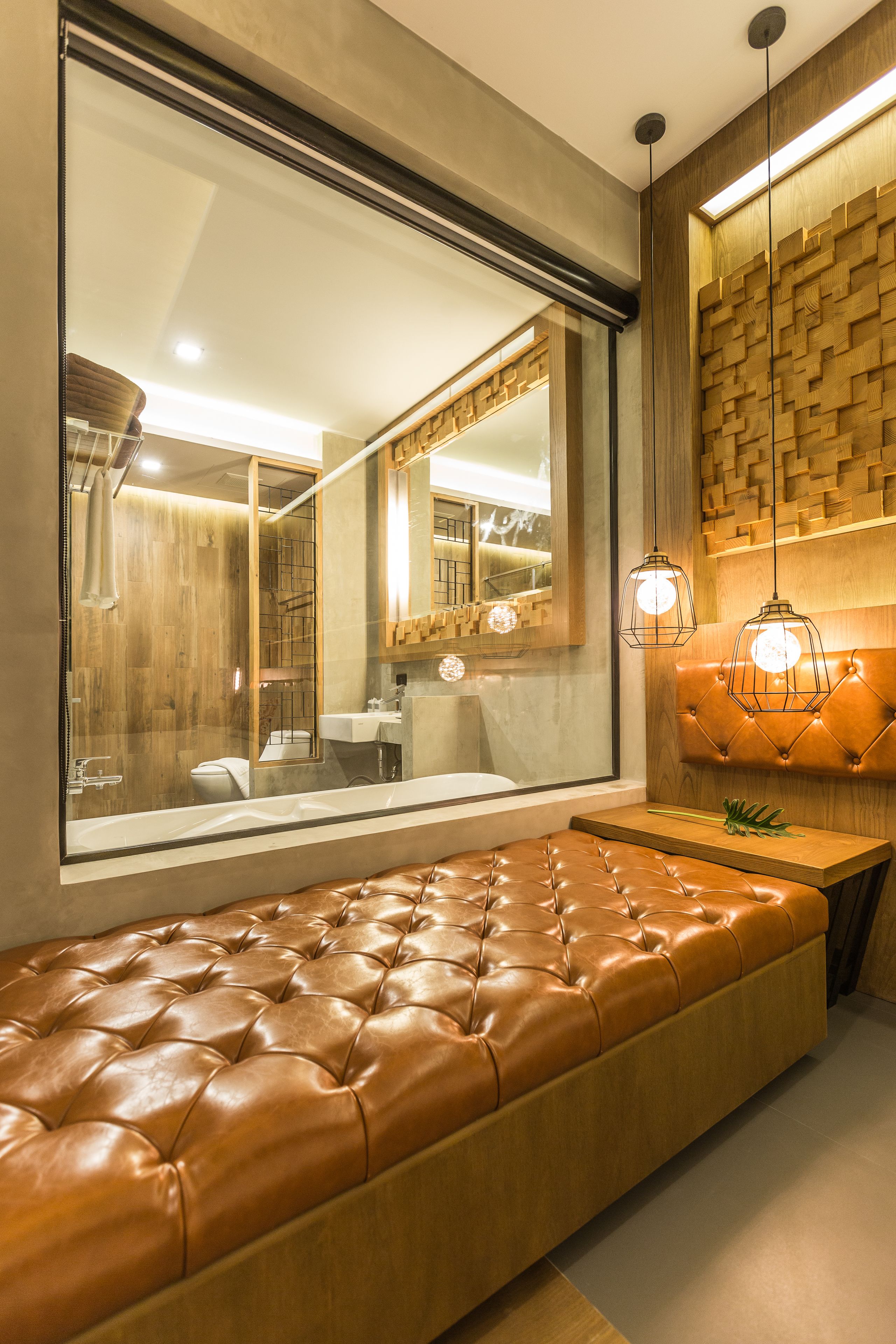 A modern bathroom with a large mirror, a wooden wall panel, a leather bench, and pendant lights.