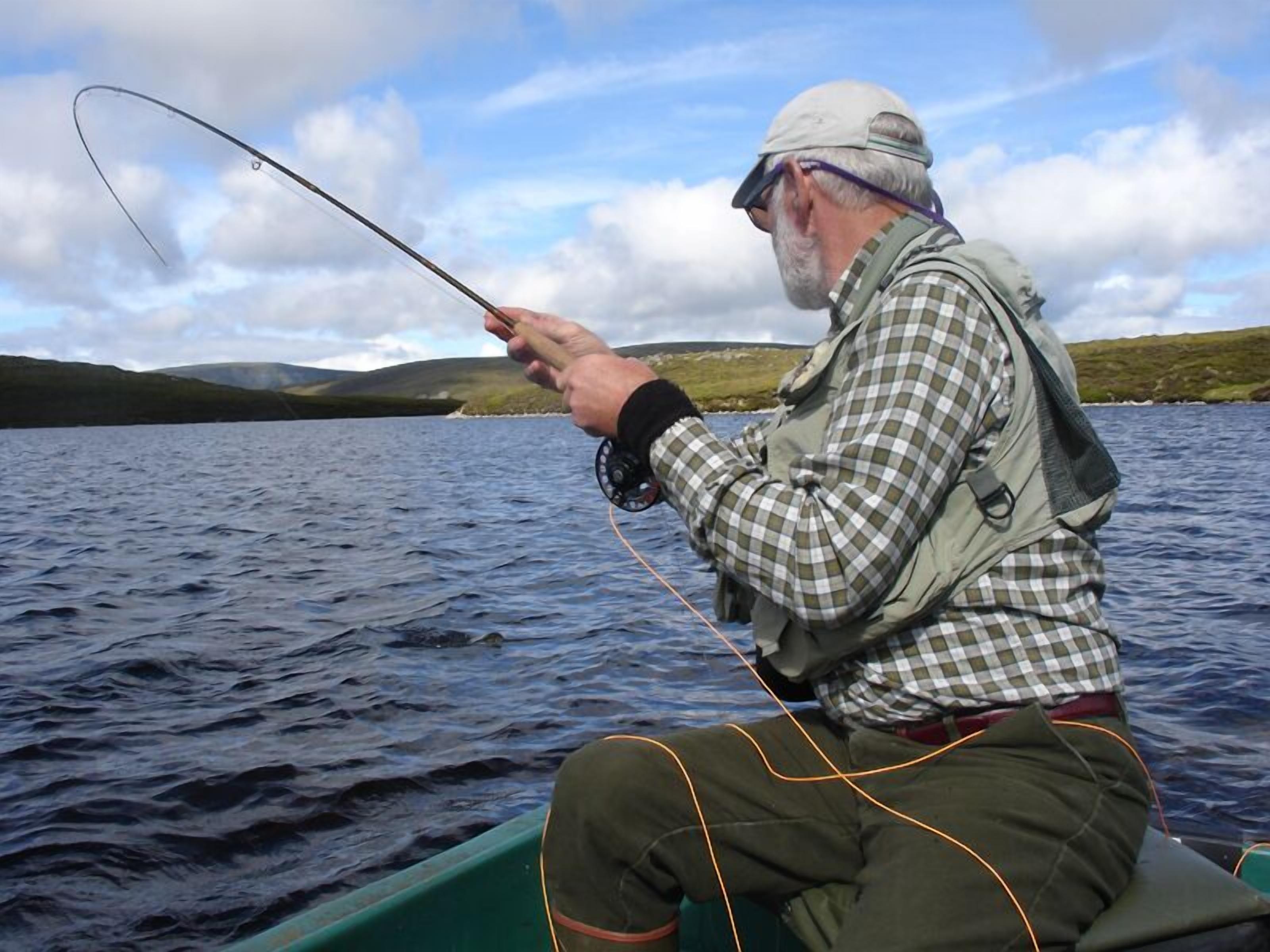 Una persona pescando en un bote en un lago, con colinas al fondo.