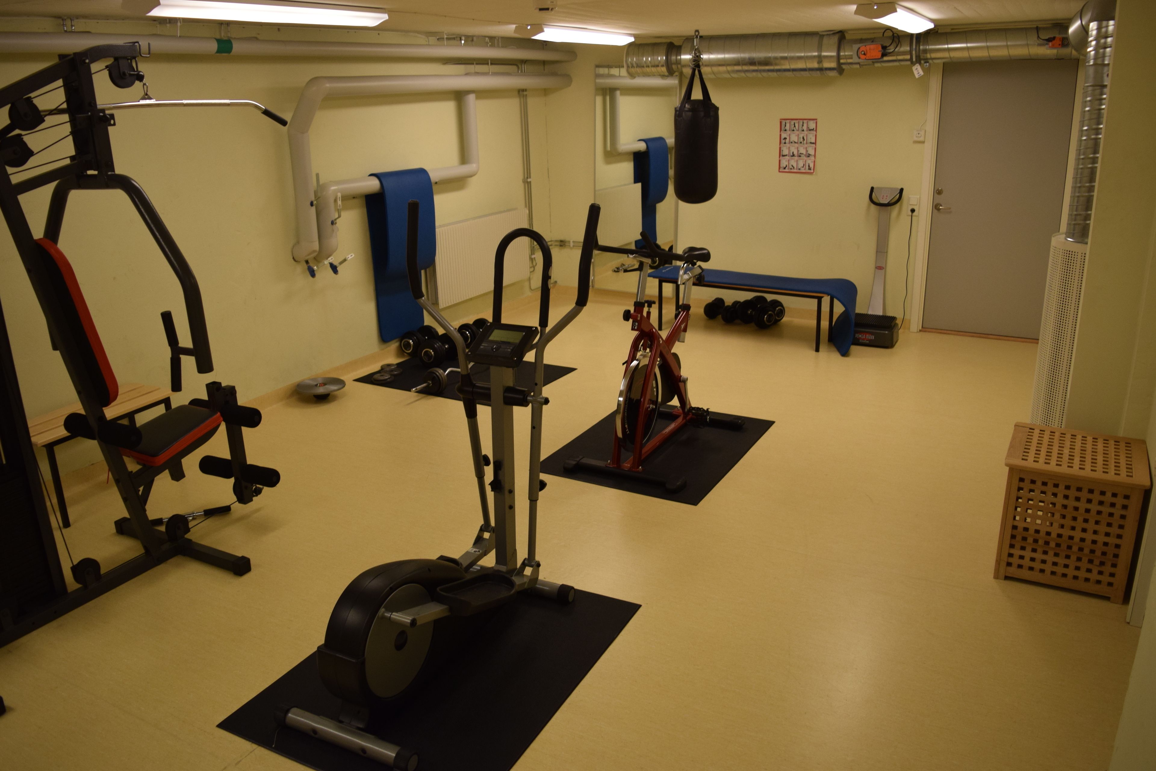 Een sportschool met trainingsapparatuur, een bank en een bokszak.