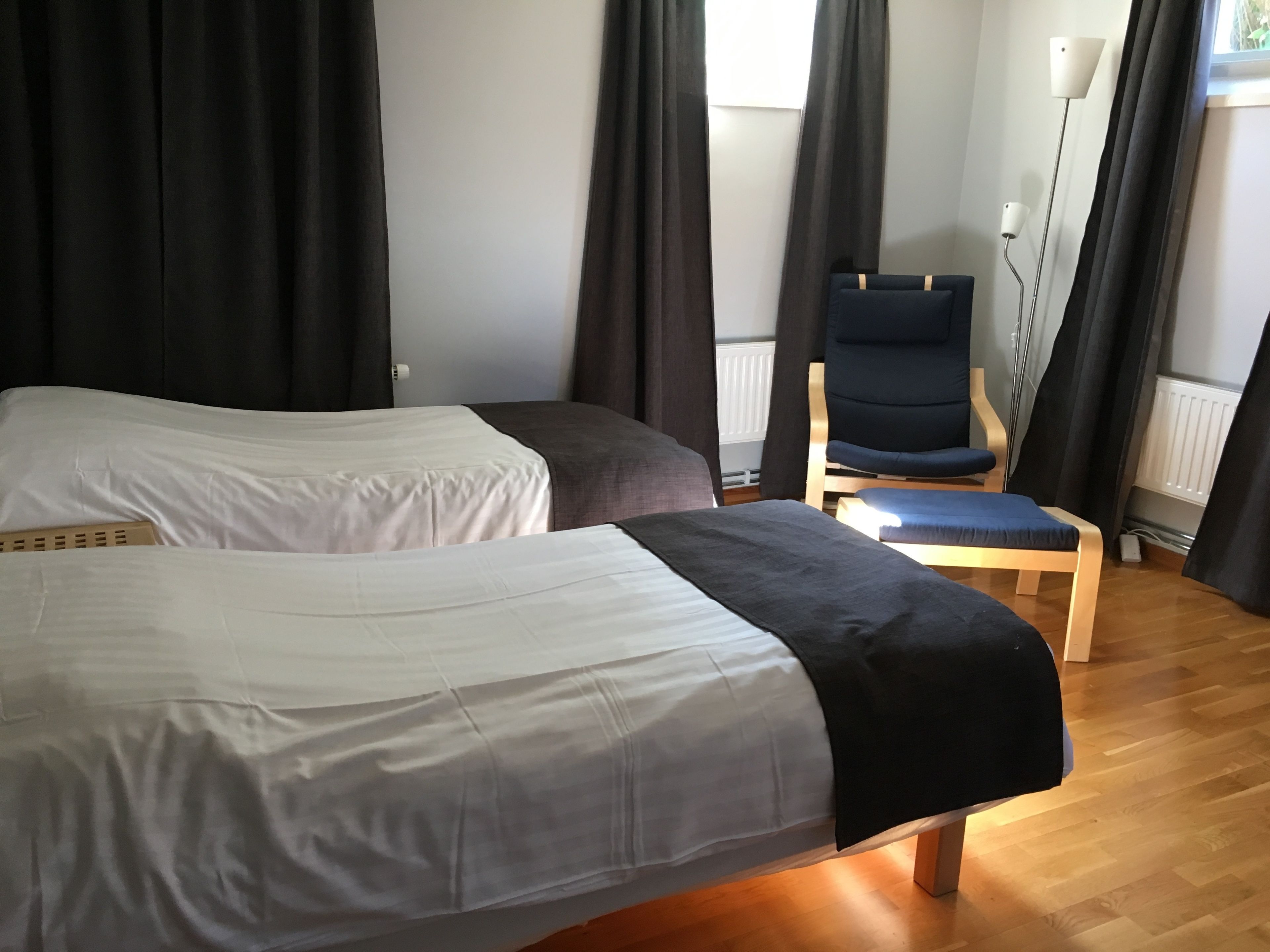 Quarto de hotel com duas camas de solteiro, uma cadeira de madeira e um abajur.