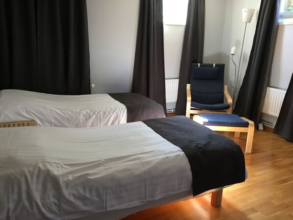A hotel room with two single beds, a wooden chair, and a floor lamp. - Hotell Hässlö (Vasteras)