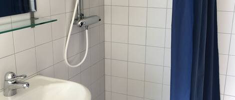Un baño con un lavabo blanco, una repisa de cristal, una ducha con manguera blanca y una cortina azul.