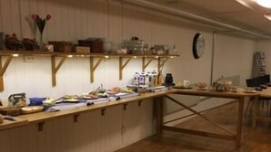 A room with a wooden floor, a long table with various items, and shelves with kitchenware.