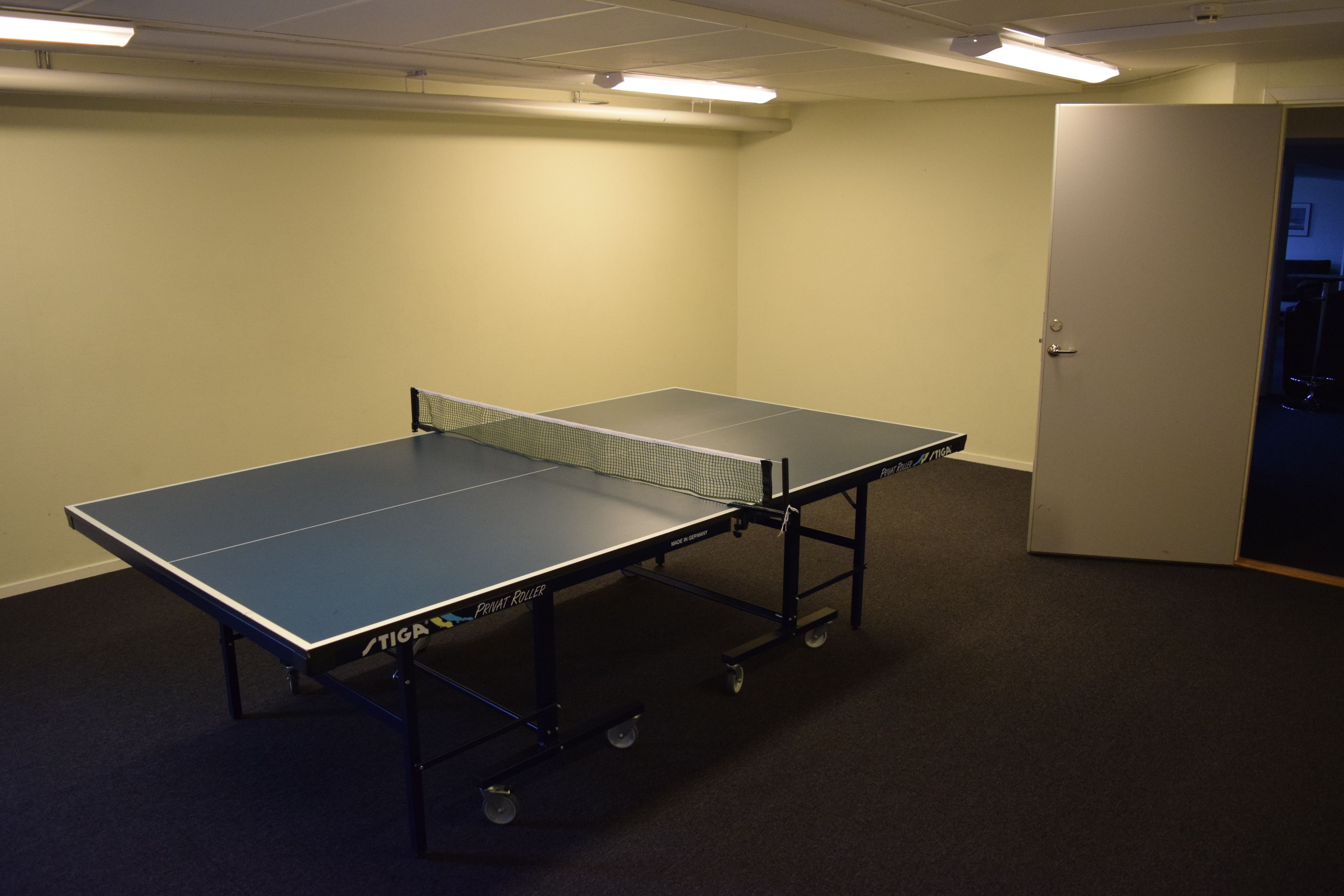 A ping pong table in a room with a door and carpeted floor.