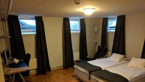A hotel room with two beds, a desk with a computer, a chair, and a window with curtains.