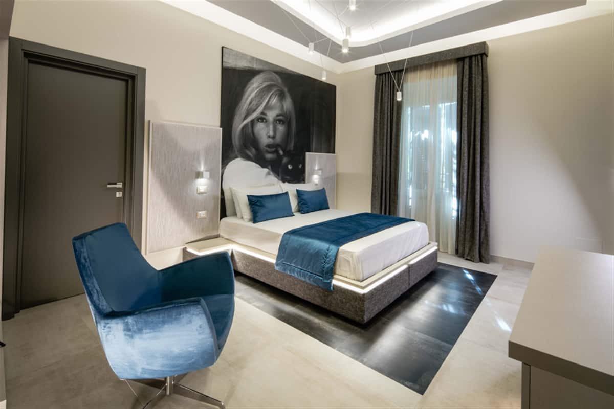 A modern bedroom with a bed, a blue chair, a large painting, and a desk.