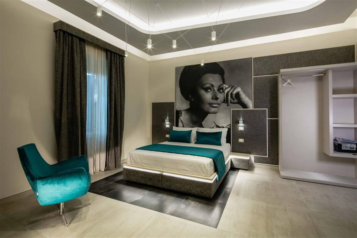 A modern bedroom with a bed, a chair, a wardrobe, and a large wall mural.