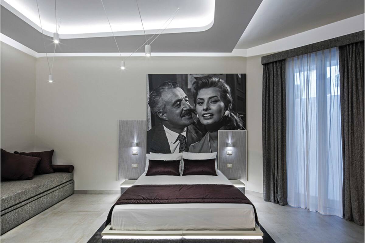 A modern bedroom with a large bed, a sofa, and a wall-mounted artwork.