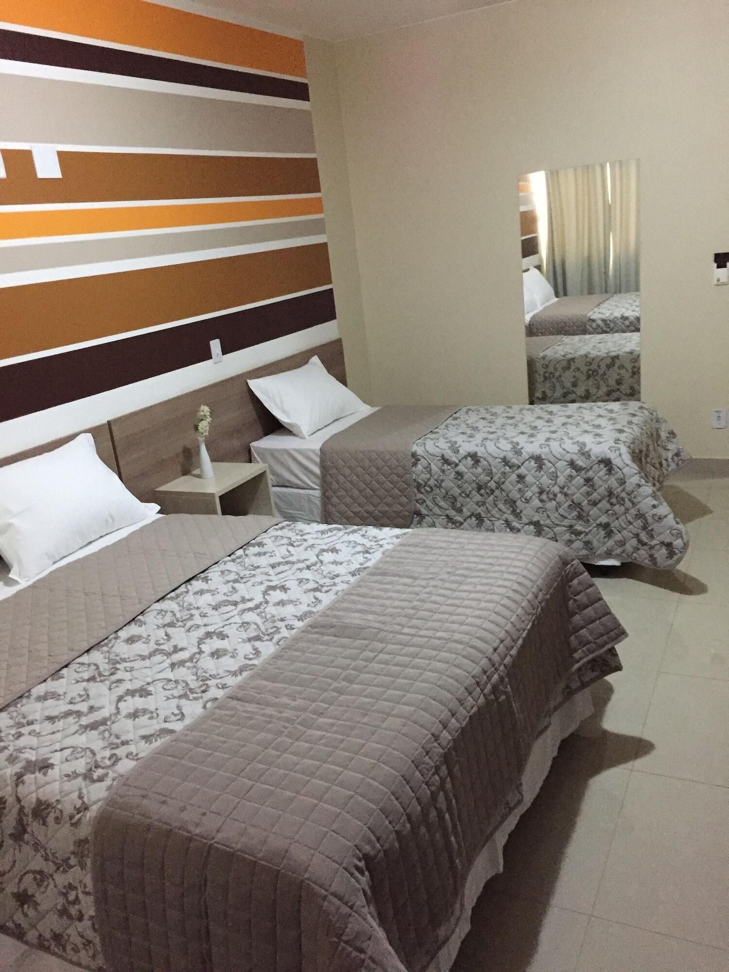 A hotel room with two beds, a striped headboard, a nightstand, and a mirror.