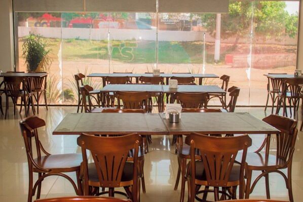 Un restaurant doté de nombreuses tables et chaises, avec de grandes fenêtres offrant une vue sur un paysage verdoyant.
