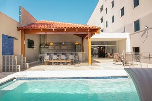 Un espace piscine extérieur doté d’un coin salon couvert et d’un bar.