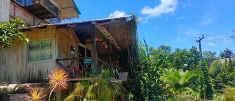 A wooden house with a balcony, a swimming pool, and lush greenery.
