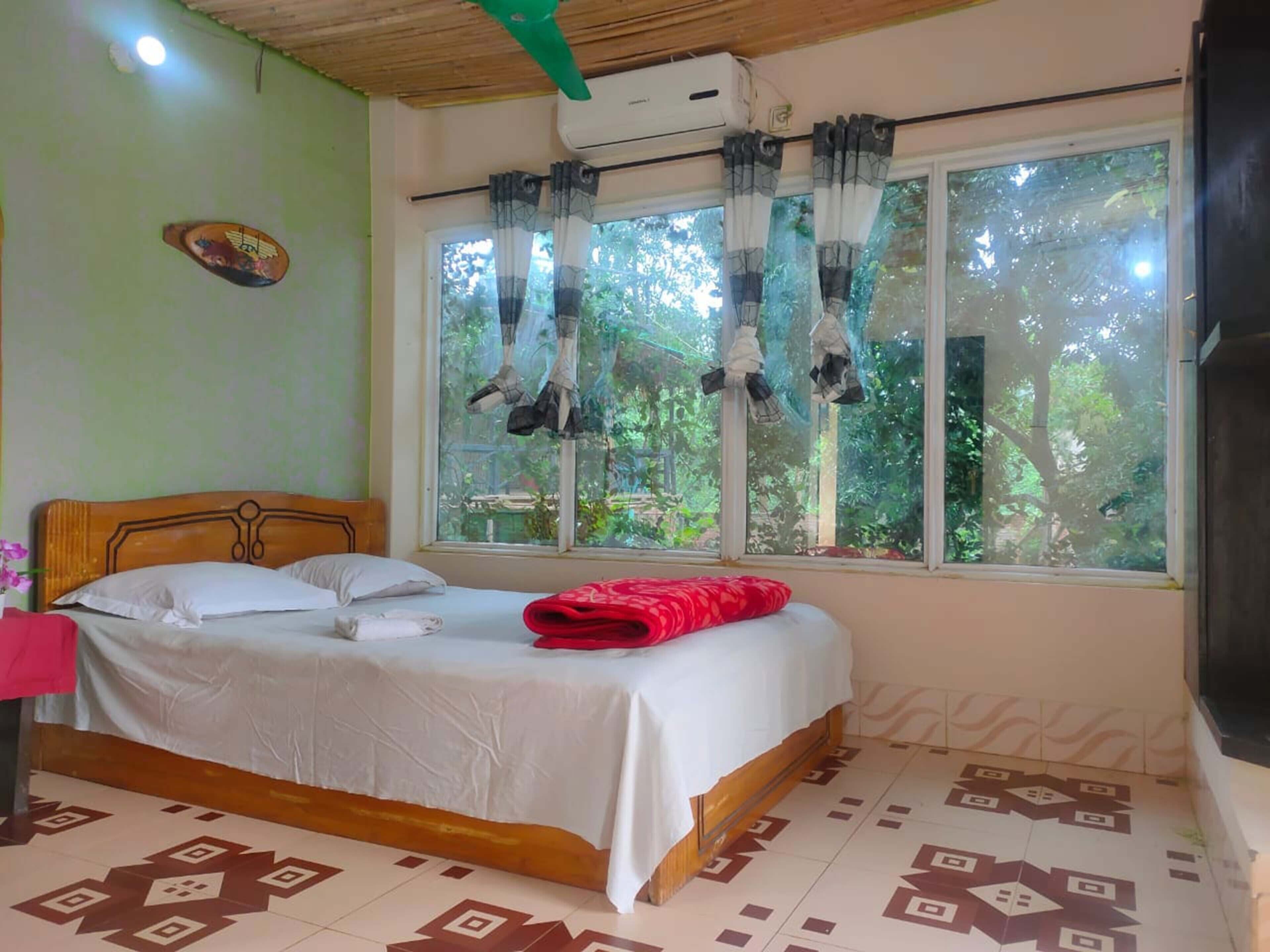 A bedroom with a bed, a window with curtains, a ceiling fan, and an air conditioning unit.