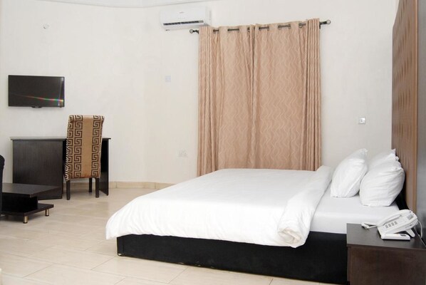 Une chambre d’hôtel avec un lit, un téléviseur fixé au mur, un bureau et une chaise.