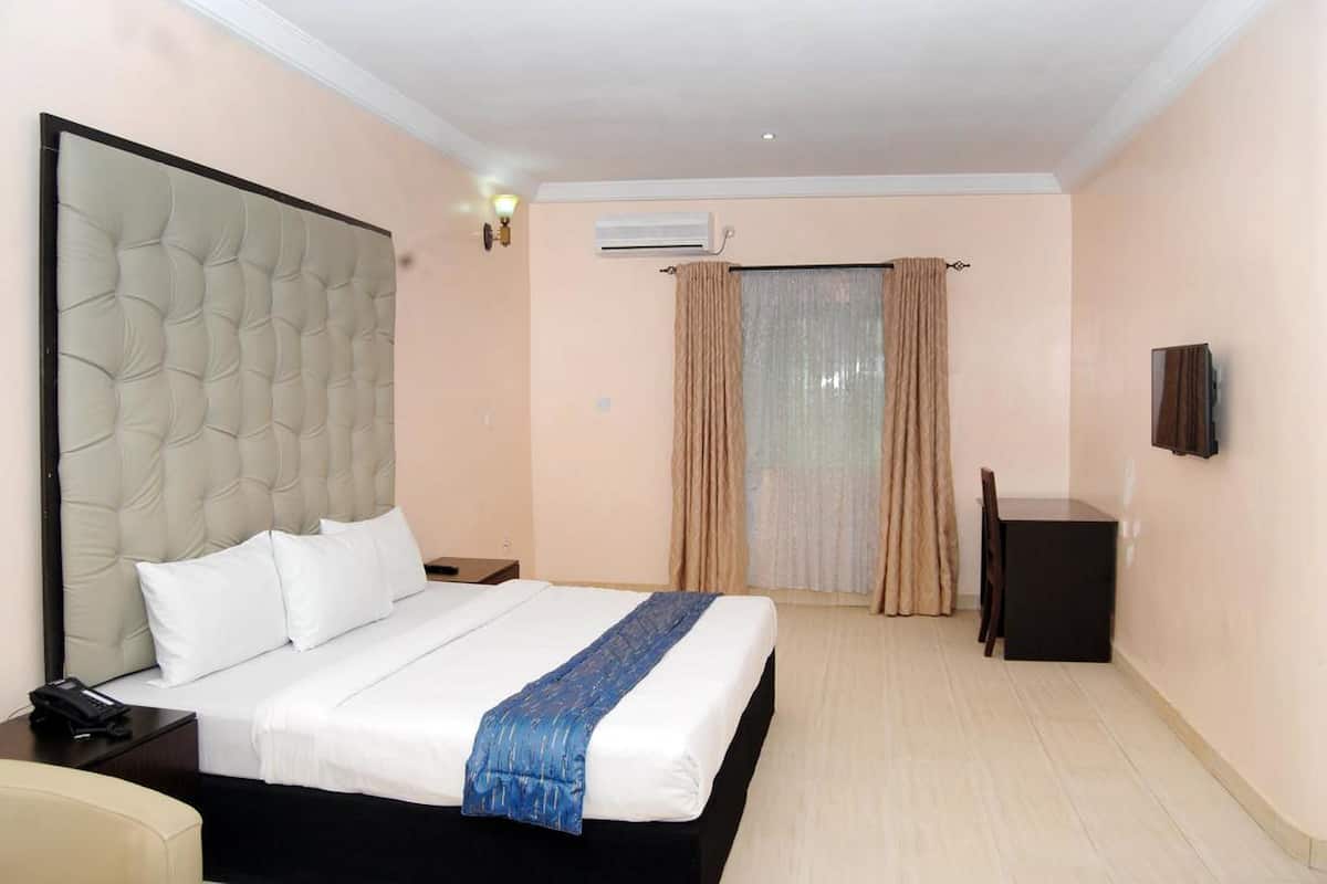 Ein Hotelzimmer mit einem großen Bett, einem Nachttisch mit Telefon, einem Schreibtisch mit Stuhl und einem an der Wand montierten Fernseher.