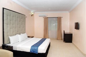 Une chambre d’hôtel avec un grand lit, une table de chevet avec un téléphone, un bureau avec une chaise et un téléviseur fixé au mur.