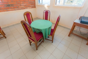 A dining area with a round table covered by a green tablecloth, surrounded by wooden chairs with red cushions.