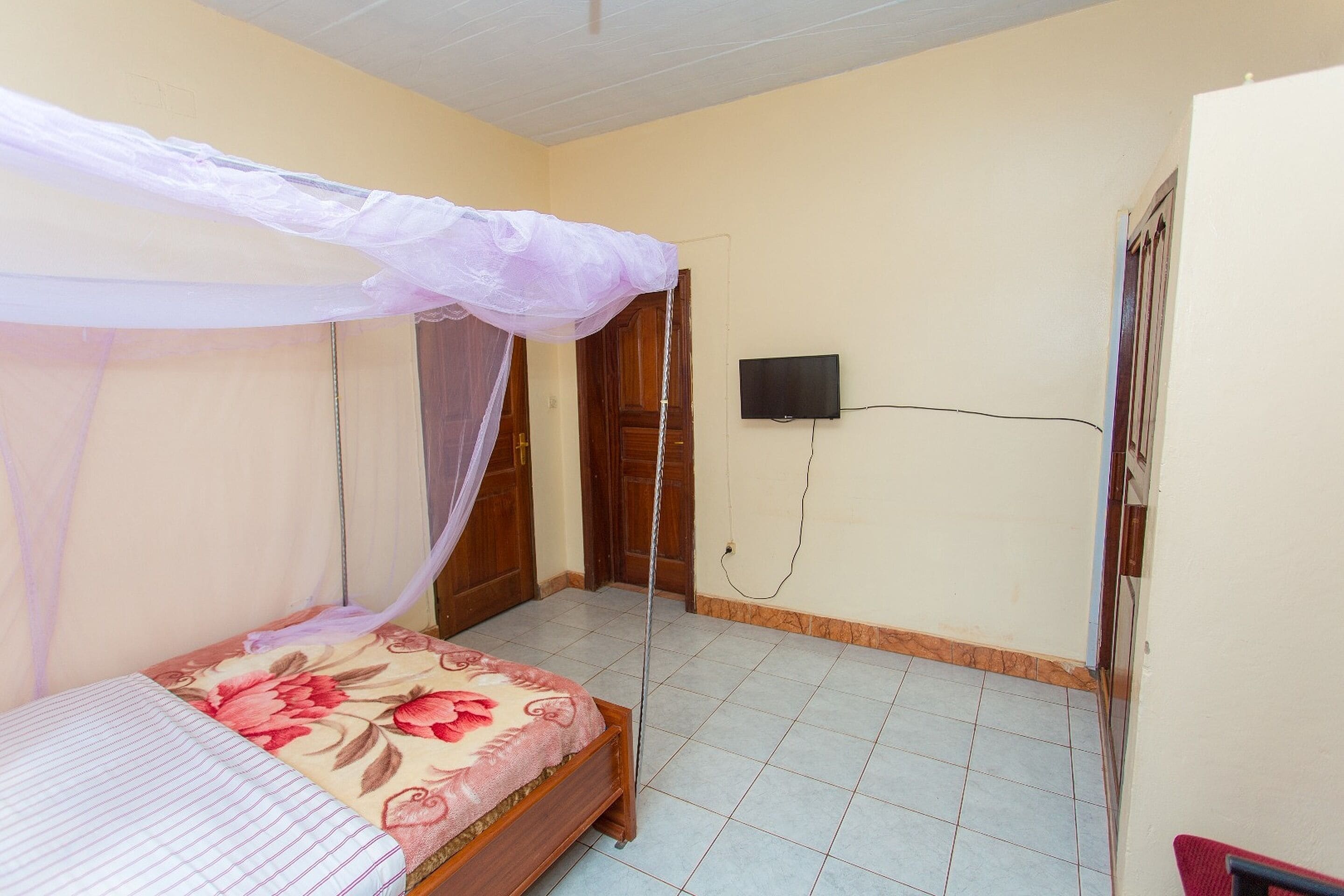 Un dormitorio con una cama bajo una mosquitera, un televisor en la pared y suelo de baldosas.