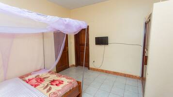 Un dormitorio con una cama bajo una mosquitera, un televisor en la pared y suelo de baldosas.