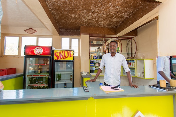 A man standing behind a counter with a refrigerator and shelves in the background.