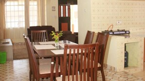 A dining area with a table and chairs, a kitchen with tiled backsplash, and a living area with a sofa and curtains.