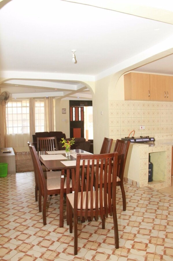 A dining area with a table and chairs, a kitchen with tiled backsplash, and a living area with a sofa and curtains.
