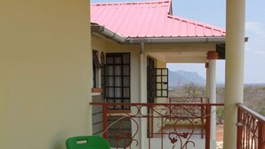 A balcony with two green chairs, a red railing, and a view of a building with a red roof.