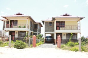 Two two-story houses with balconies, a car parked in front, and a gravel driveway.