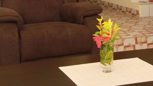 A living room with a brown sofa, a glass vase with flowers, and a staircase with red railings.