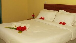 A neatly made bed with white linens and red flowers, a wooden headboard, and a small bedside table with a red flower vase.