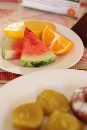 A plate with watermelon, orange, and a slice of yellow fruit, possibly mango, on a tablecloth. - Merry Villa Hotel & Apartments (Mtwapa)