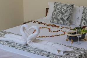 A neatly made bed with patterned pillows, a decorative towel, a bowl with a plant, and a wine glass. - Merry Villa Hotel & Apartments (Mtwapa)