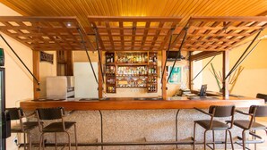 Zona de bar con techo de madera, barra con una variedad de botellas y dos taburetes.