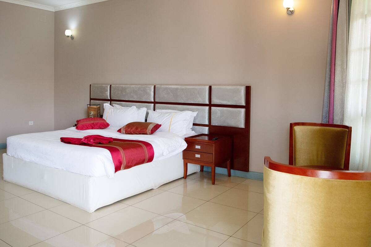 A hotel room with a large bed, a nightstand, a chair, and a wall-mounted light.