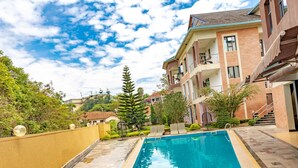 A swimming pool with a clear blue water, surrounded by a yellow wall and a brick building with balconies. - Orient Park Hotel (Kigali)