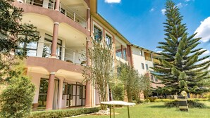 A multi-story hotel with balconies, a well-maintained garden, and a large coniferous tree. - Orient Park Hotel (Kigali)