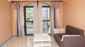 A living room with a sofa, a white coffee table, and a sliding glass door leading to an outdoor area. - Orient Park Hotel (Kigali)