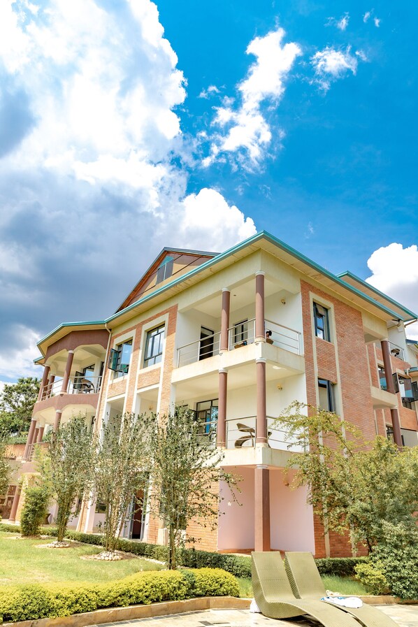 A multi-story building with balconies, a garden area, and a clear blue sky with clouds. - Orient Park Hotel (Kigali)