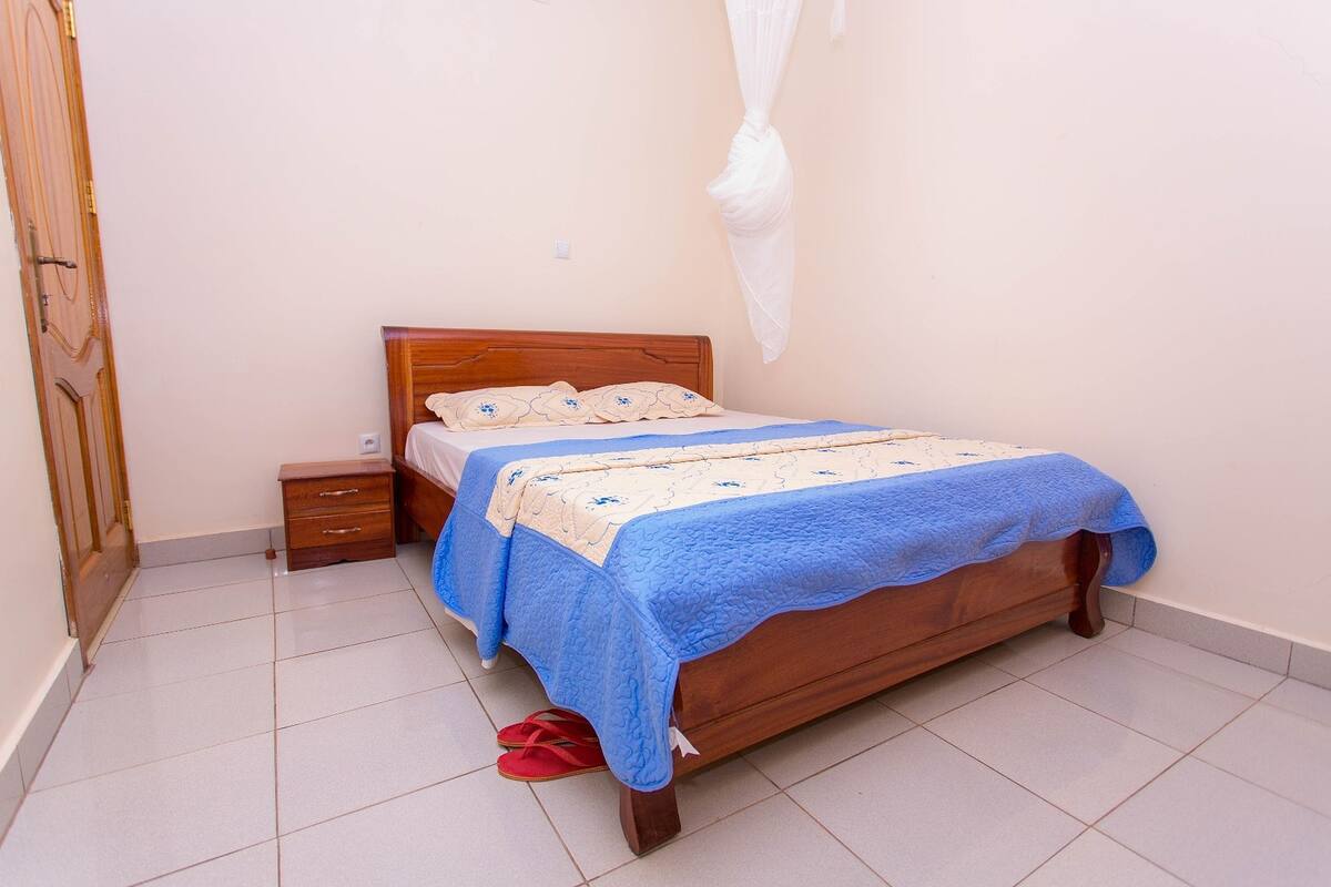 A bedroom with a wooden bed, a nightstand, a drawer unit, and a white mosquito net.